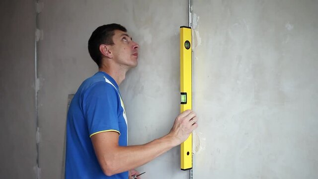 A male builder applies a yellow level to the wall. Align curved walls with beacons. Renovation in the house.