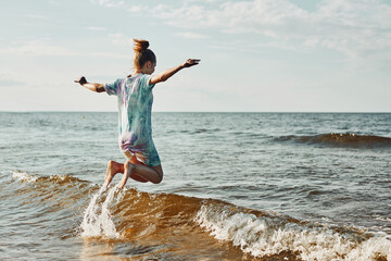 Girl enjoying sea jumping over waves spending a free time over sea on a beach at sunset during summer vacation