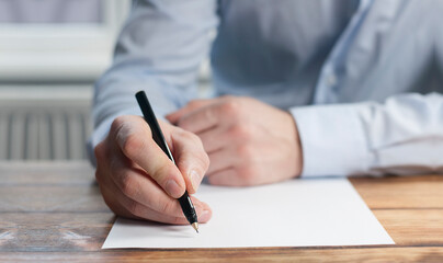 The hand of a businessman writes with a pen on a white sheet of paper. In the office