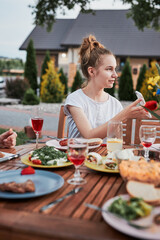 Family having a meal from grill during summer picnic outdoor dinner in a home garden. Close up of people sitting at a table with food and dishes