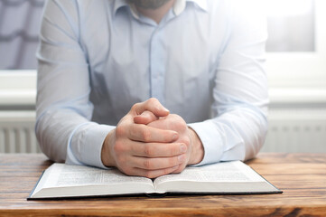 Obraz premium Open Bible book on the table. The man holds his hand on the Bible. Prayer to God. Hands are praying