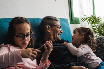 Grandfather and his two granddaughters, watching the mobile phone on the sofa.