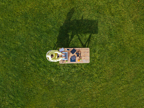Aerial view of woman working on laptop at coffee table set on green lawn