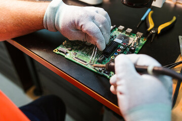 Technician soldering circuit board of electrical component at workbench in electronics repair shop