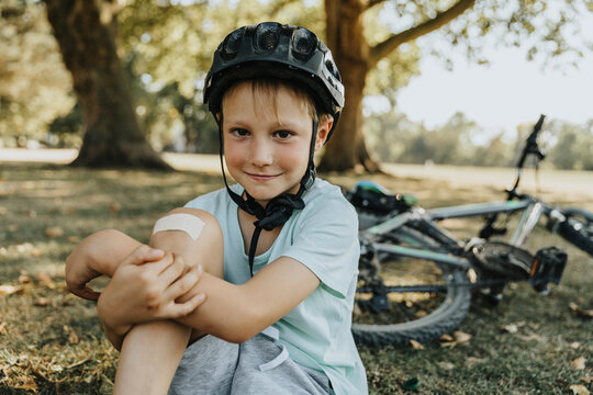 Boy sitting with bandage on knee in pubic park on sunny day