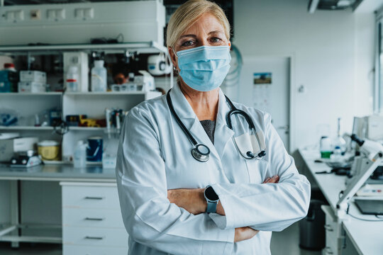 Confident scientist wearing face mask standing with arms crossed at laboratory
