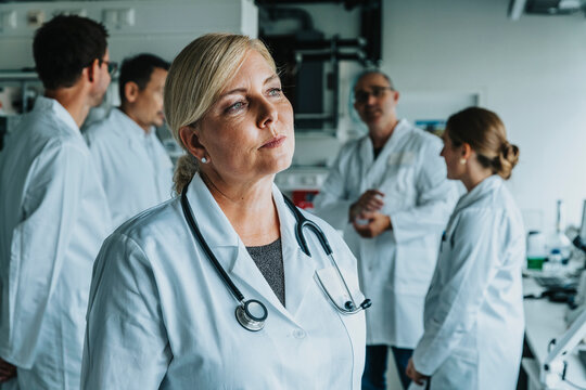 Female scientist looking away while standing with coworker in background at laboratory