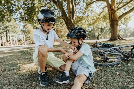 Boy putting bandage on younger brother knee sitting in public park
