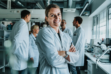 Smiling woman with arms crossed standing with coworker in background at laboratory