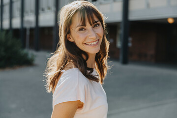 Mature woman smiling while standing on street during sunny day
