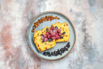 top view raisin cake slices with raisins and raspberries on blue oval plate on marble ground with copy space