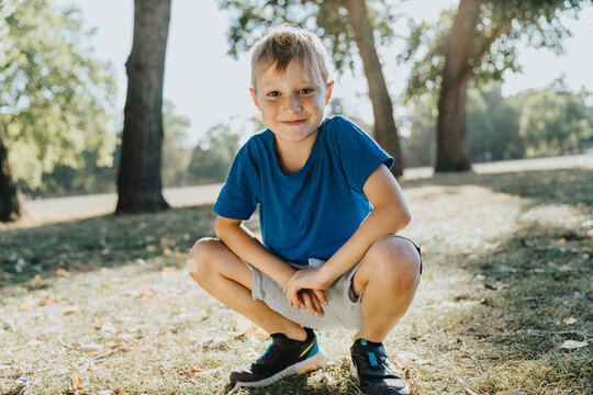 Smiling boy crouching in pubic park on sunny day