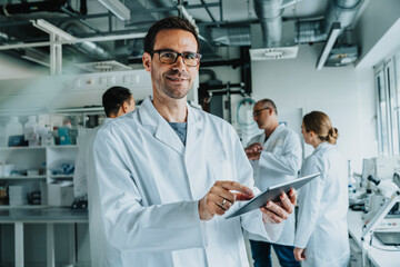 Smiling male scientist using digital tablet while standing with coworker in background at laboratory