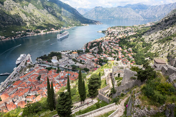 Fototapeta na wymiar Panoramic view of the Kotor Gulf or Boka Kotorska with medieval town, sea port with ferryboats and surrounding mountains. View from the walls of fort. Montenegro, Europe