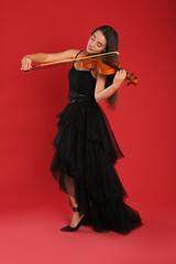 Beautiful woman playing violin on red background
