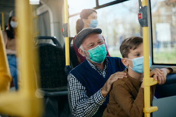 Happy grandfather with grandson commuting by bus during COVID-19 pandemic.