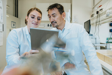 Assistant and scientist using digital tablet while sitting at laboratory