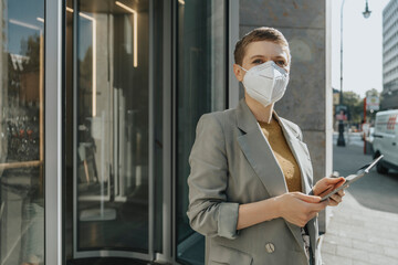 Woman wearing protective face mask using digital tablet while standing on street in city