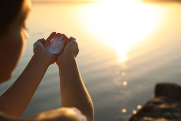 Woman with feather outdoors on sunset, closeup. Healing concept