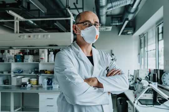 Confident scientist wearing face mask standing with arms crossed at laboratory