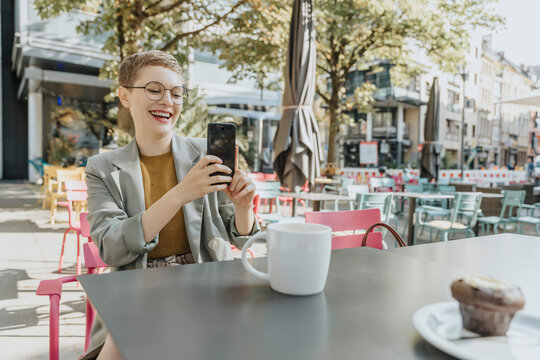 Woman taking selfie on smart phone while sitting in outdoor cafe