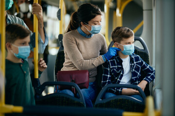 Caring mother adjusting son's protective face mask while commuting by public transportation.