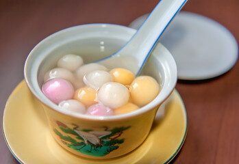 Close up top side view of red, orange and white tangyuan (tang yuan, glutinous rice dumpling balls) 
in white bowl on wooden background for Winter solstice festival food.
