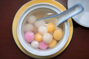 Close up top view of red, orange and white tangyuan (tang yuan, glutinous rice dumpling balls) in white bowl on wooden background for Winter solstice festival food.