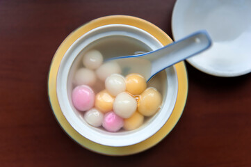 Close up top view of red, orange and white tangyuan (tang yuan, glutinous rice dumpling balls) in white bowl on wooden background for Winter solstice festival food.