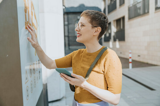 Mid adult woman reading map while holding smart phone standing in city on sunny day