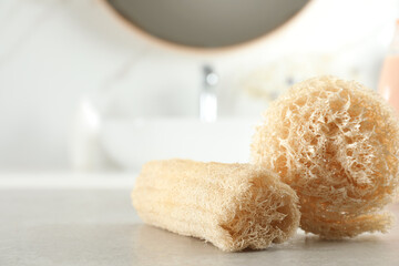Natural loofah sponges on table in bathroom, closeup. Space for text