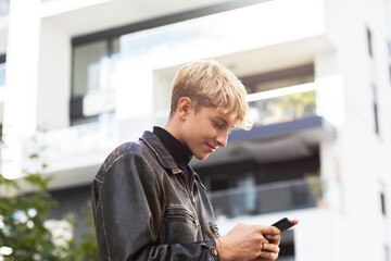 Blond teenage boy using smart phone in city