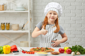 little girl in chef hat and an apron cooking pizza in the kitchen. child showing Ok gesture. delicious