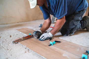 Male manual worker installing parquet flooring in house