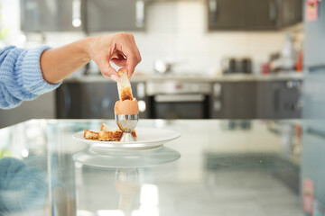 Woman dipping toast in boiled egg at home