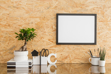 Desk with blank picture frame on wooden wall.