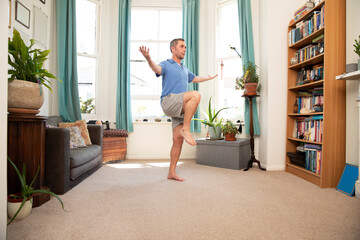 Mature man balancing on leg while standing at home