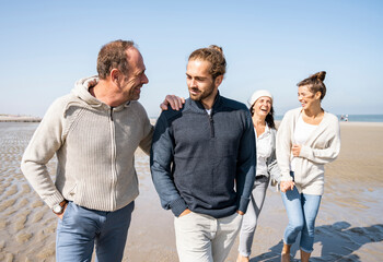 Men talking while walking with women in background at beach