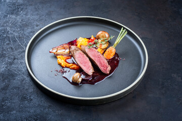Modern style traditional wild hare back filet braised with wild berries and red wine jus with mashed carrot puree and sweet potato served as close-up on Nordic design plate