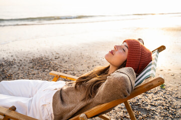 Young woman relaxing on folding chair with eyes closed at beach during sunset