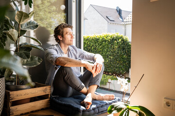 Mid adult man sitting on cushion at home on sunny day