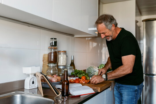 Smiling mature man cutting vegetable while standing in kitchen at home