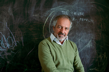 Mature man sitting by blackboard at home