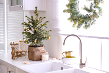 Small Christmas tree decorated with baubles and festive lights in kitchen