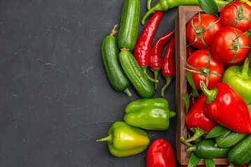 Half shot of fresh vegetables inside and outside of a brown wooden basket on the left side on dark background close up view