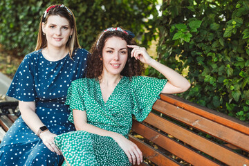 Smiling beautiful female friends sitting on bench at park