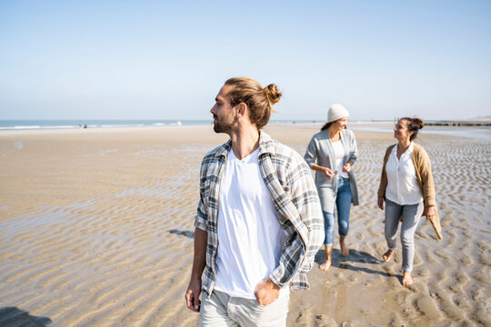 Man looking away while walking with women talking in background at beach