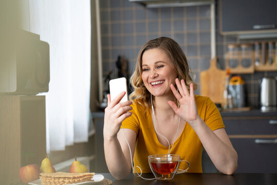 Happy woman having a video chat with smartphone in kitchen at home