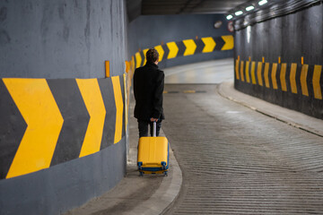 Man with a rolling suitcase in a parking. Man in underground car parking garage