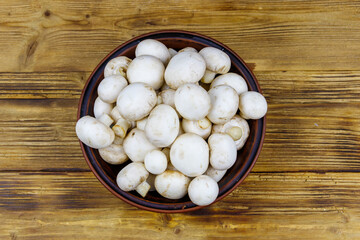 Fototapeta na wymiar Fresh champignon mushrooms in ceramic bowl on the wooden table. Top view
